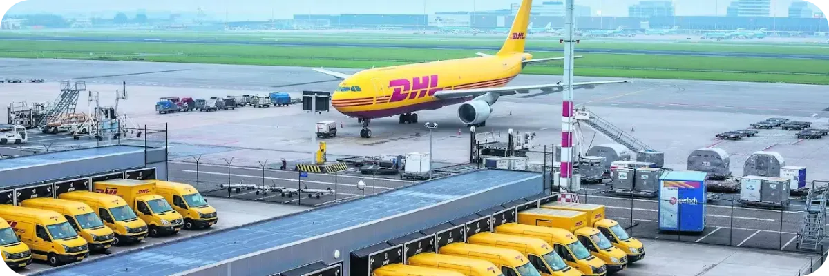 Yellow DHL cargo aircraft on the apron with a row of yellow vans in front of it