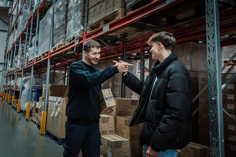 Two Djops colleagues bump fists between the racks in a warehouse