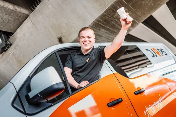 Smiling Djops colleague raises his arm out of the window of an orange and white company van