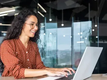 Smiling woman with glasses behind a laptop in an office