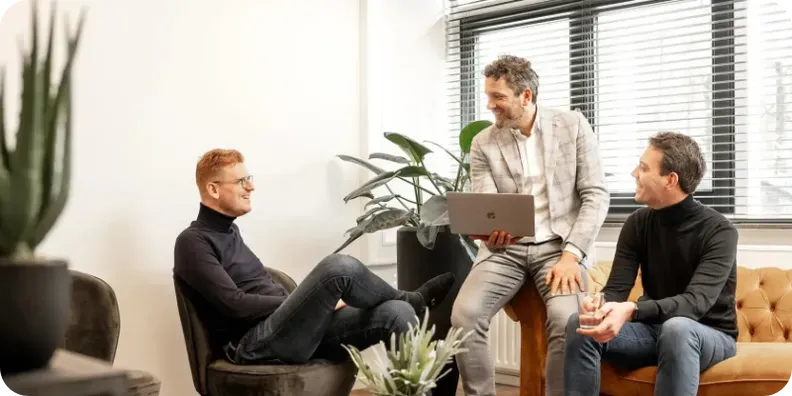 Three Faam colleagues in conversation in a bright office space, one of them with a laptop on their lap