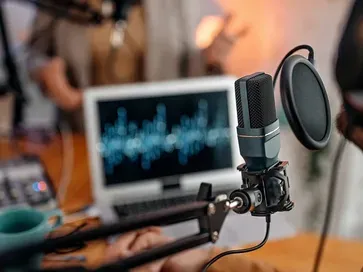 Podcast microphone with pop filter in front of a screen showing a sound wave
