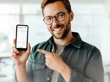 Smiling man with glasses pointing at a smartphone showing a dashboard
