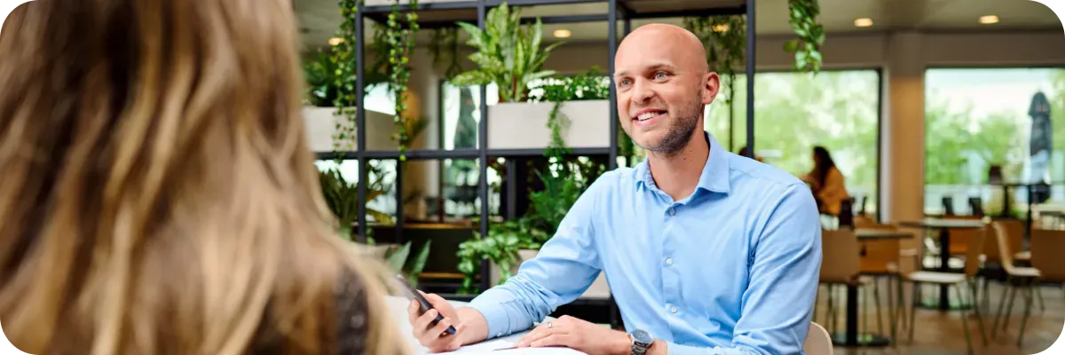 Smiling Schiphol colleague in a blue shirt in conversation at a table in a green staff canteen