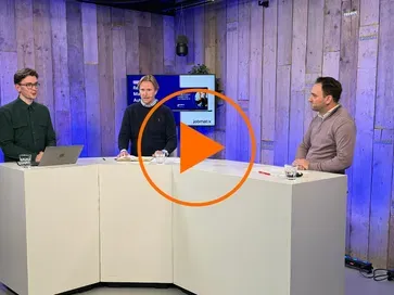 Three speakers at a study table during the recording of the webinar, with a play button over the image